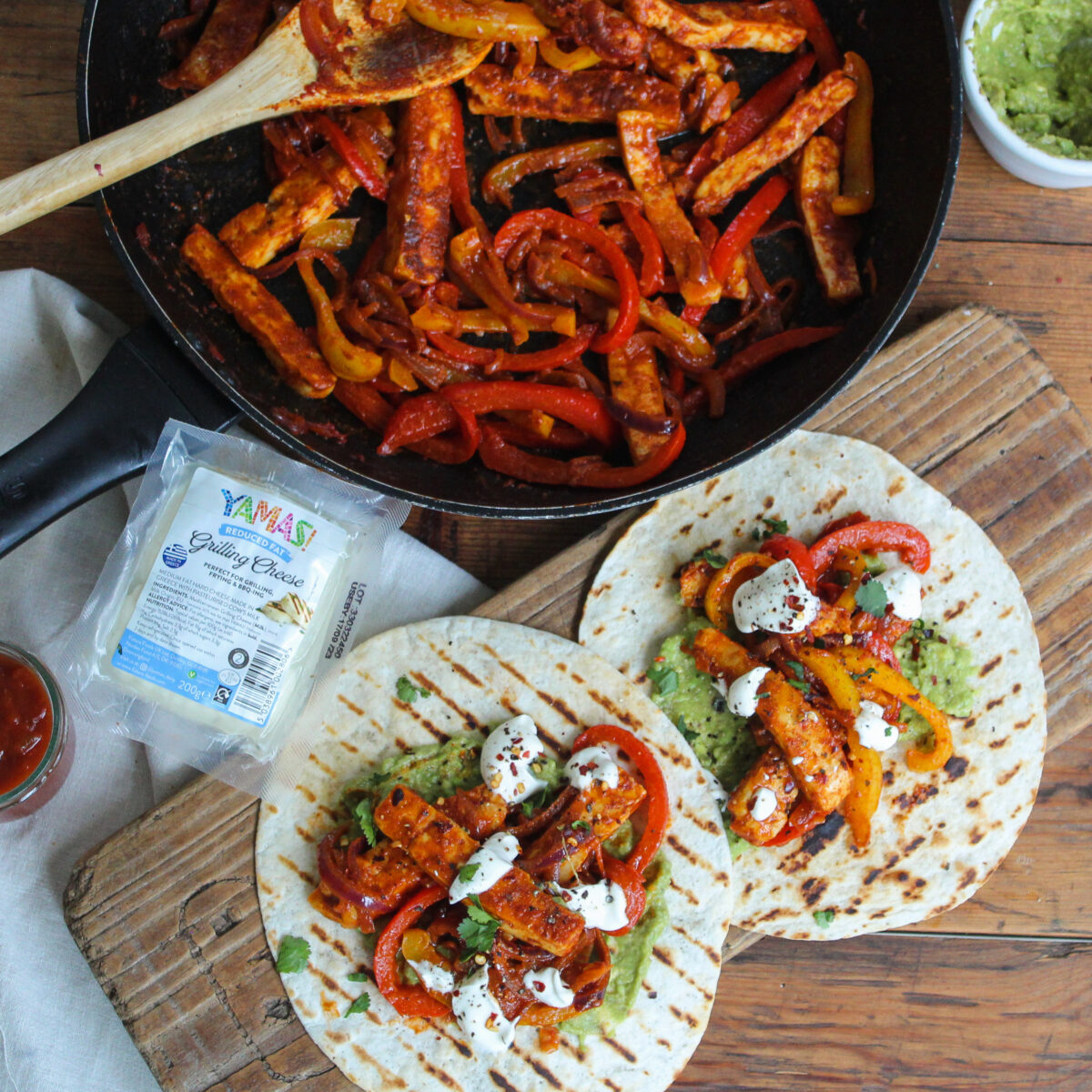 Tortilla wraps topped with fried grilling cheese, vegetables, sour cream and guacamole on a chopping board